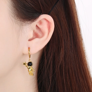 Close-up of a golden astronaut earring featuring a black helmet visor on a model's ear