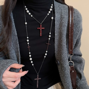 Detail einer mehrlagigen Perlenkette mit roten Strass-Kreuzanhängern auf dunklem Pullover