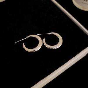 Macro shot of silver C-shaped hoop earrings with polished finish on black velvet background