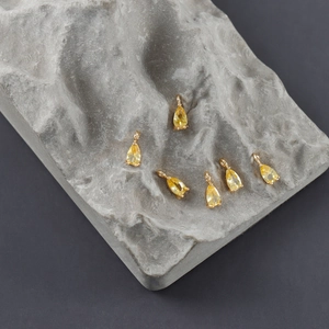 Vista macro de seis colgantes de circón chapados en oro en forma de pera sobre piedra gris