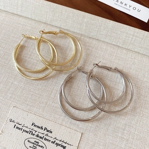 Detail of gold and silver multi-layer textured hoop earrings on beige fabric background
