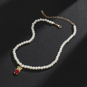 Detail view of pearl necklace featuring golden bear pendant with red heart gemstone