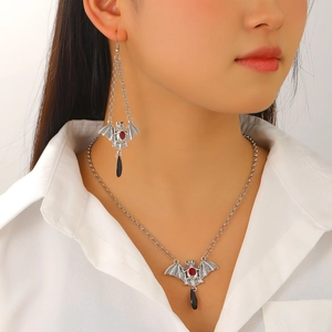 Detail view of silver gothic bat necklace and earrings set with red gems on a model