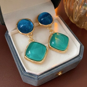 Vintage gold-plated earrings with blue round and green square stones on blue velvet