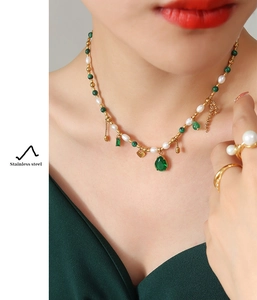 Detail of elegant stainless steel gold chain necklace with green gems and pearls