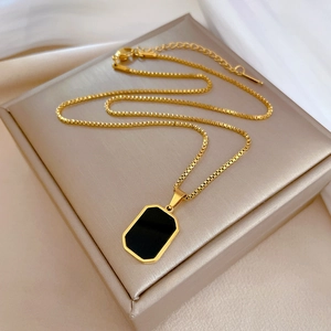 Macro detail of gold-plated box chain and black geometric pendant on silk texture