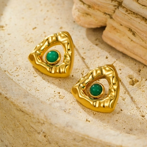 Macro view of gold triangular earrings with green stone on natural stone background