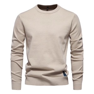 Détail d'un pull beige à col rond avec poignets côtelés et étiquette bleue au bas