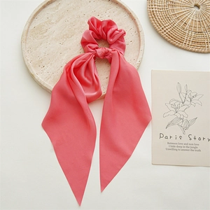 Detail of coral satin scrunchie with long ribbons on a marble tray with artistic decor