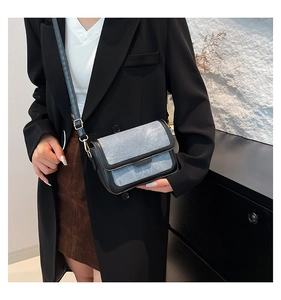 Detail of light blue denim and black leather crossbody bag with golden hardware
