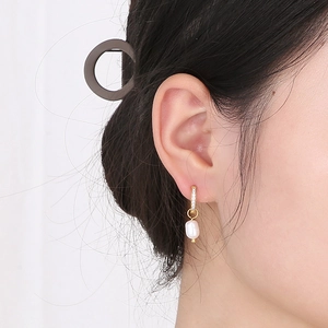 Détail d'une femme portant une boucle d'oreille en or 18K avec perle et zircons