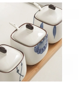 Detailed view of three ceramic spice jars with lids and spoons on a wooden tray