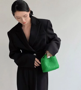 Detailed close-up of green woven leather bucket bag carried by model in black blazer