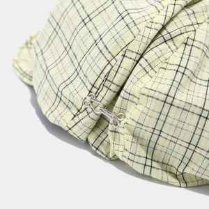 Detail of silver metal hook fastener on yellow plaid fabric beret with fine stitching