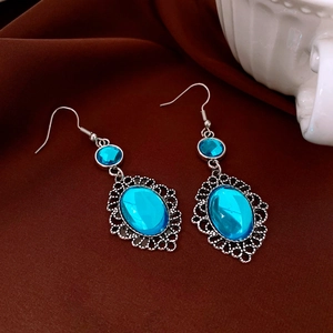 Dettaglio di orecchini boho in resina blu con filigrana d'argento su tessuto di seta
