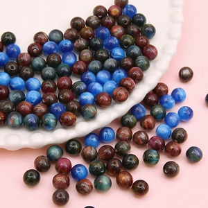 Mix of 8-12mm resin beads in blue and gold brown scattered on a ceramic plate for DIY