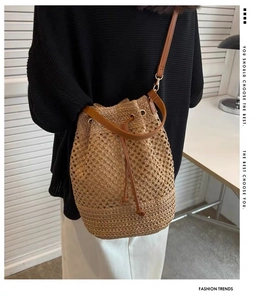 Detail of handwoven straw bucket bag with brown faux leather drawstring and shoulder strap