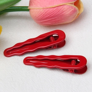 Detail of two glossy red wavy metal hair clips with smooth finish on white fabric