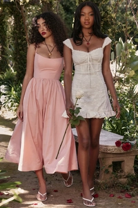 Detail of pink backless midi dress and white lace mini dress in a sunlit garden setting
