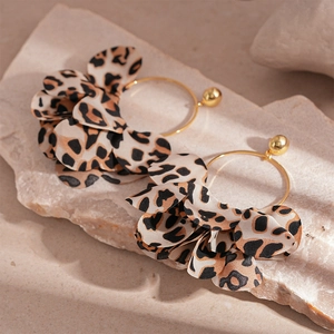 Detailed close-up of leopard print fabric petals on golden hoop earrings set on stone