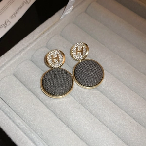 Close-up of golden rhinestone H-letter stud earrings with dark grey fabric pendants