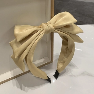 Elegant cream satin triple bow headband with black trim on a white marble surface