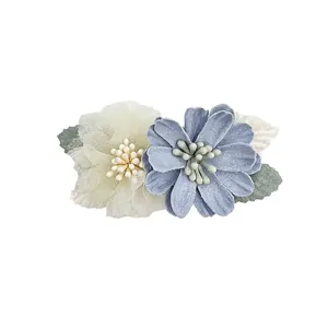 Detail view of light blue fabric and cream mesh flower hair clips with green leaves