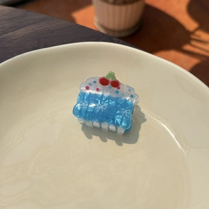 Cute cake shaped hair claw in sea blue acrylic with cherry detail on a ceramic plate