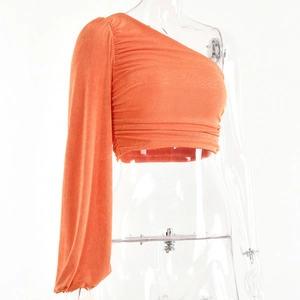 Détail d'un haut orange à une épaule avec texture plissée et design à une manche longue