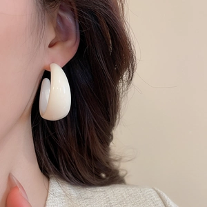 Gros plan d'une grande créole en acrylique blanc crème en forme de C sur une oreille