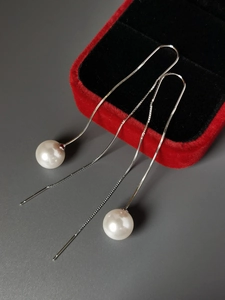 Dettaglio di orecchini lunghi in argento con perle bianche su sfondo di velluto rosso