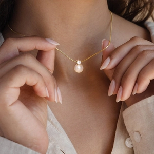 Detailed close-up of a pearl pendant necklace with gold chain on model's hand