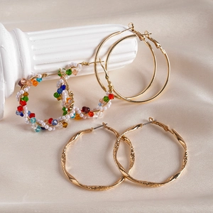 Détail de créoles dorées torsadées et boucles d'oreilles perles sur tissu en soie