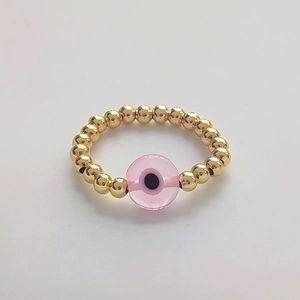 Macro shot of 18K gold beaded ring with pink evil eye glass bead on white background