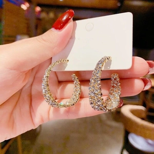 Détail macro des créoles dorées en forme de C serties de strass avec tiges en argent S925