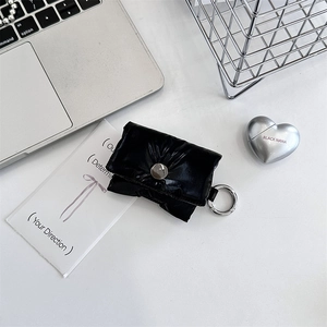 Close-up of black quilted puffer headphone case with metallic ring hook on white desk