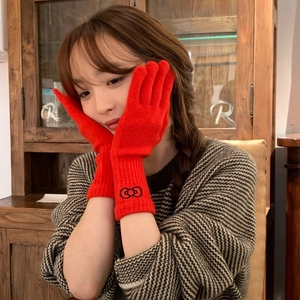 Red knit gloves with black bow patterns worn by model in a cozy vintage setting