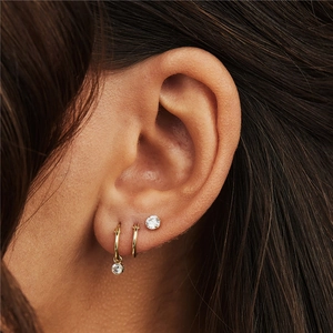Detailed view of layered gold hoop earrings with zircon pendants on model's ear