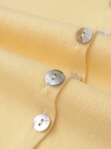 Gros plan des boutons en nacre et de la maille fine du débardeur en tricot