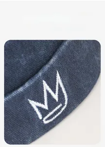 Close-up of white crown embroidery on navy blue knit docker cap with fine texture