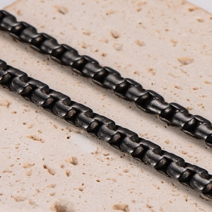 Sleek black stainless steel box chain necklace for men on a textured beige stone background