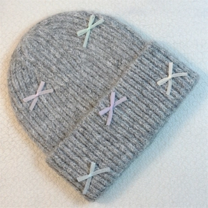 Detail of grey knitted beanie with colorful ribbon bows on soft white plush background