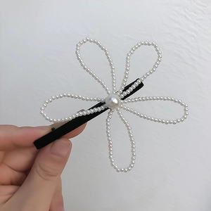 Elegant white pearl flower hair clip with black clasp held against a plain white background