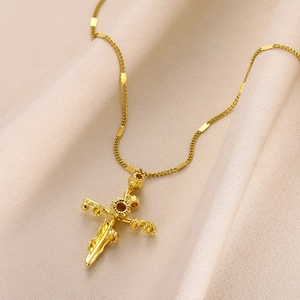 Detail shot of a gold-plated floral cross necklace resting on soft silk fabric