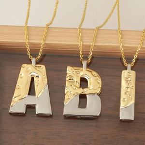 Two-tone gold and silver alphabet pendant necklaces A B I on a dark wooden background