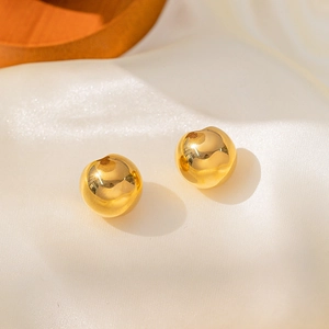 Polierte goldene Kugelohrringe auf beige Seidenstoff mit minimalistischem Design