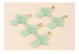 Close-up of five light green cross pendants with golden metal clasps on beige background