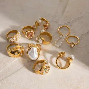 Golden stainless steel rings set with white pearls and colorful zircons on stone surface
