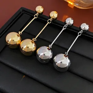 Minimalist gold and silver spherical drop earrings displayed on a black leather stand