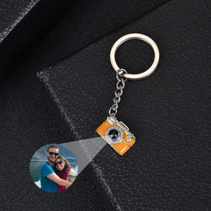 Orange camera-shaped metal keychain with personalized photo projection on black surface